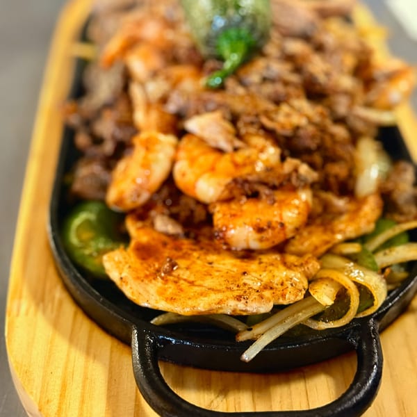 Sizzling Rancho Alegre fajitas with chicken, shrimp, steak, onions, and bell peppers on a cast iron skillet.