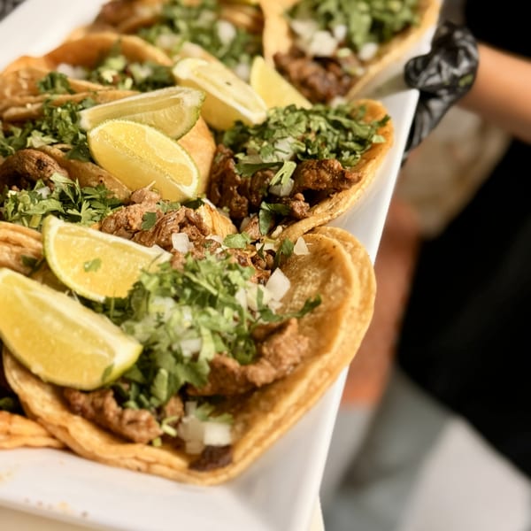 A white platter of Rancho Alegre's Mexican tacos, garnished with cilantro, onions, and lime wedges.