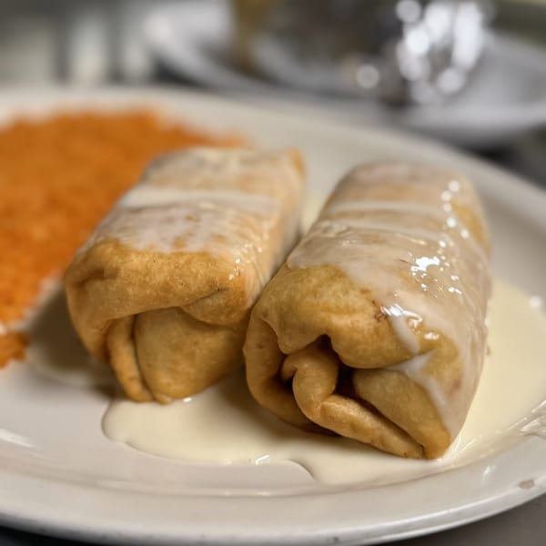 Two golden-brown Mexican burritos, drizzled with white sauce, on a white plate with orange rice.